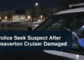 Investigator examines damaged cruiser windshield wipers with the headline Police Seek Suspect After Beaverton Cruiser Damaged