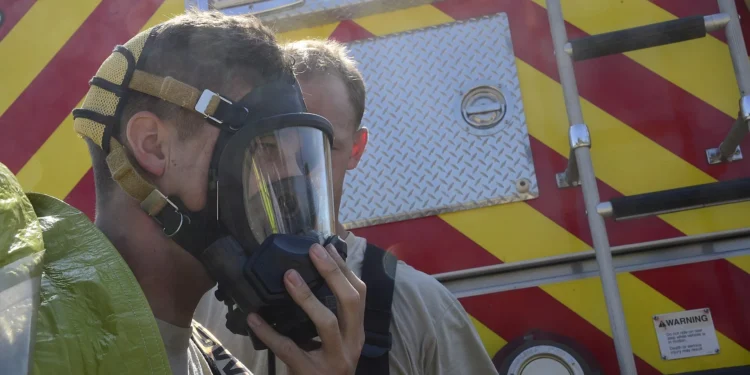 File photo: Two firefighters in protective suits, one helping the other adjust a respirator mask, in front of a fire truck during a hazardous materials training exercise. Representative image; does not show the Uxbridge exercise.