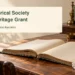 Original editorial illustration of a blank archival ledger, cotton gloves and a storage box on a wooden table, not a photograph of the society.